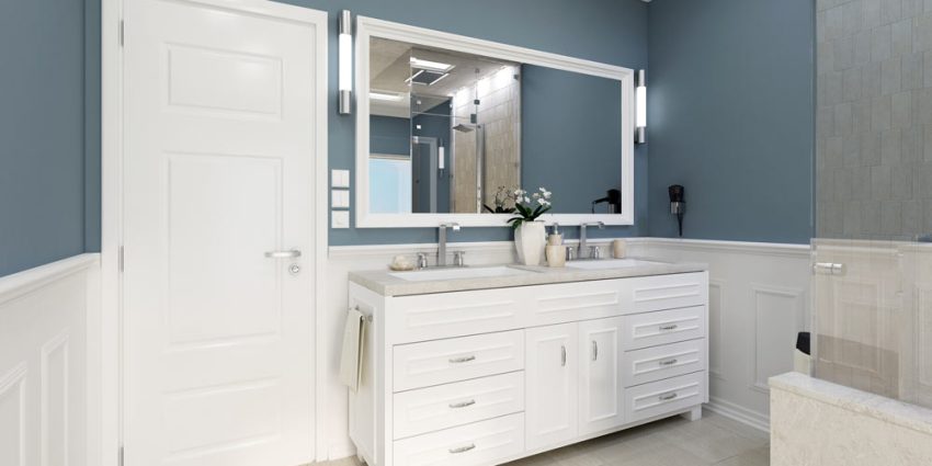 A bright and spacious bathroom featuring a modern double vanity with two polished chrome faucets. The vanity has a white marble countertop with a rectangular sink basin in each sink. Mounted on the wall above the vanity is a large rectangular mirror with a brushed nickel frame. To the left of the sink is a white hairdryer. Light colored tiles line the walls and floor, creating a modern and fresh atmosphere.