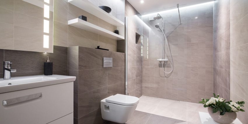 A modern bathroom remodeled with a toilet, sink, and shower. The shower has a glass door and the floor is tiled.